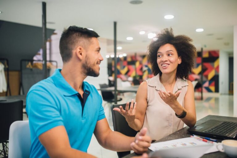 Smiling young people sharing office desk and talking