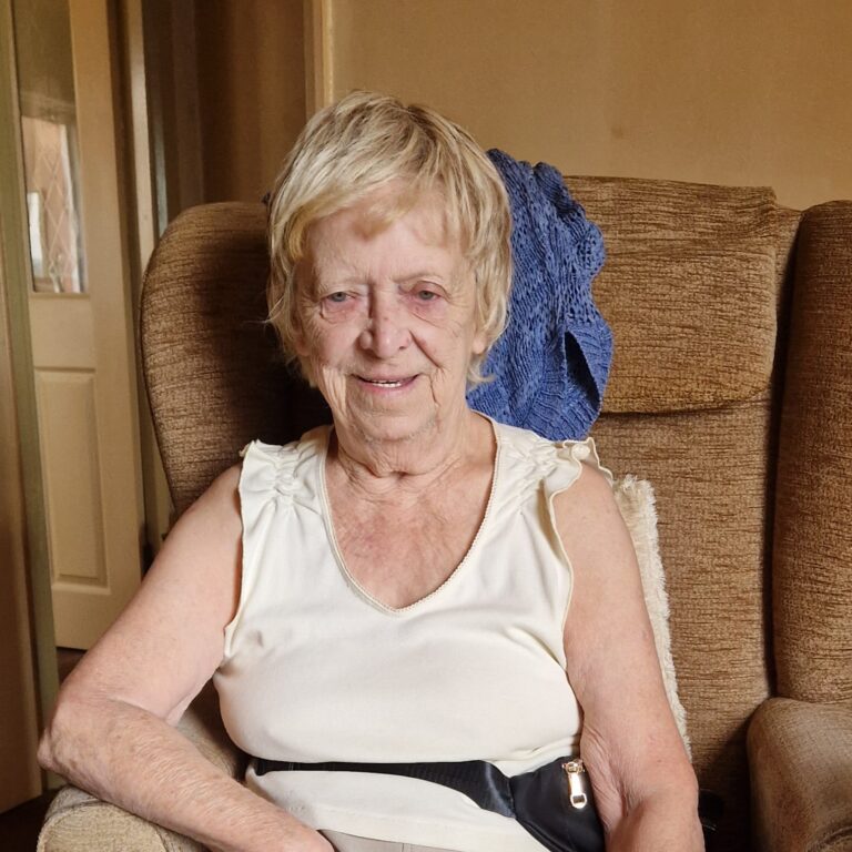 Pam wearing a white top, sat in a brown chair.