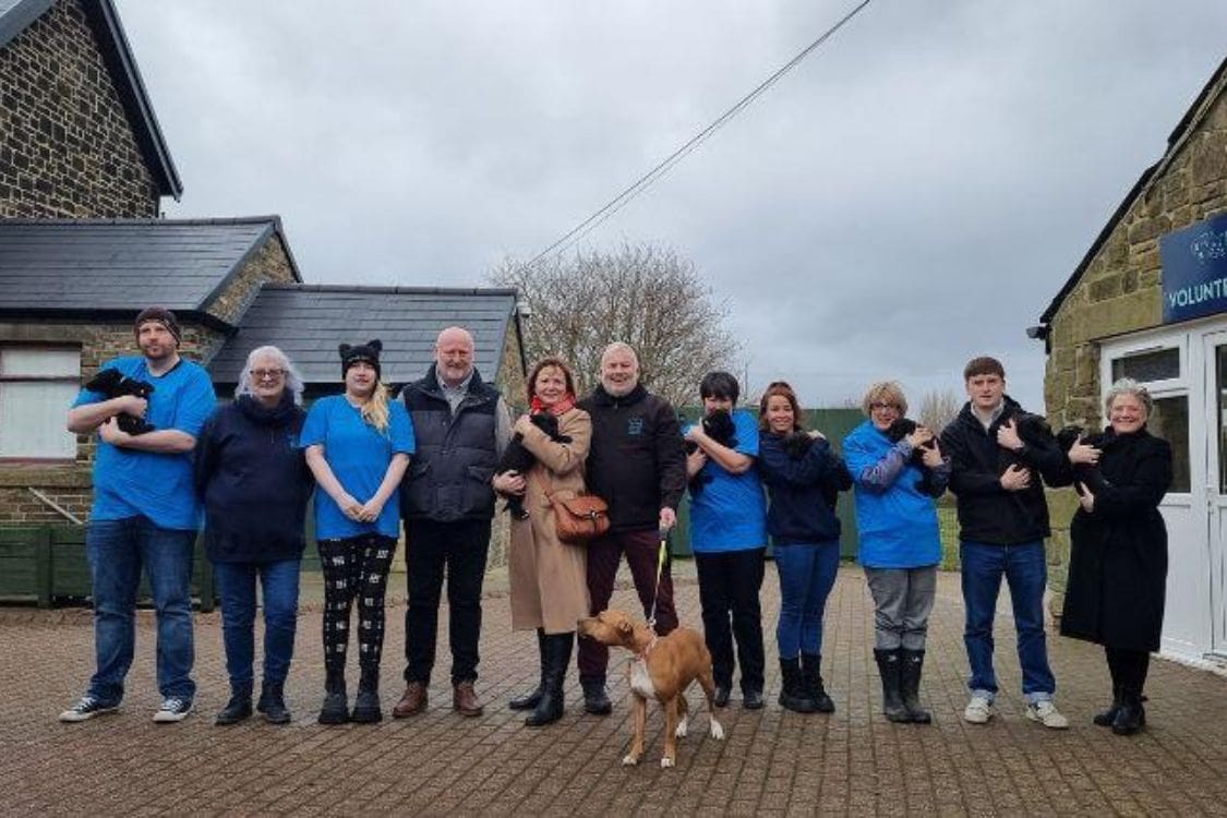 Large group of people dressed mainly in blue and black standing in front of the new building at the Newcastle Dog & Cat shelter. A number of them are holding cats and dogs.