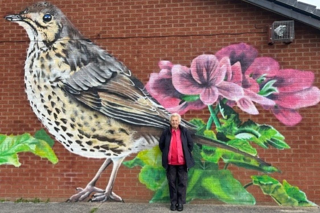 A person standing next to a mural of a bird
