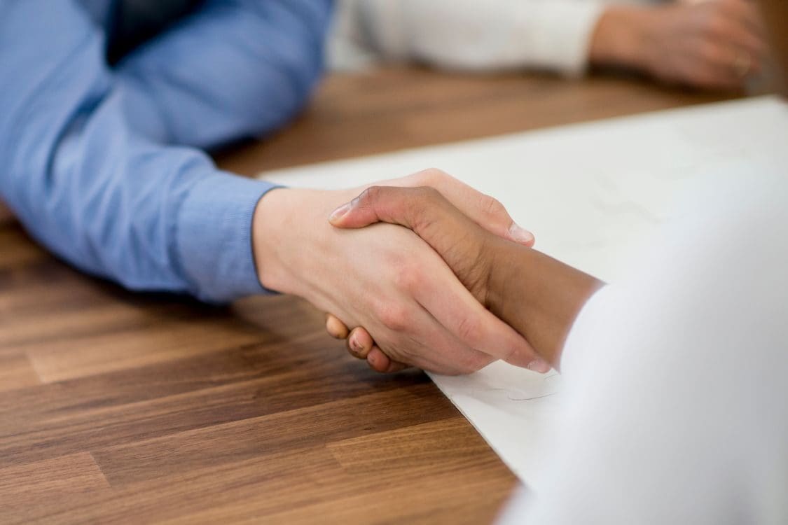 Two people shaking hands over a wooden table, symbolizing agreement and partnership, with a focus on the hands, one in a blue sleeve.